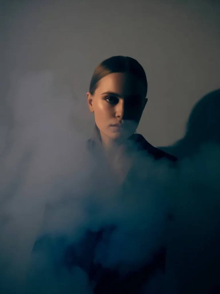 Moody editorial shot of the Eilish perfume bottle with low lighting, a charcoal or deep blue background, and subtle smoke or shadow effects creating a dramatic atmosphere.